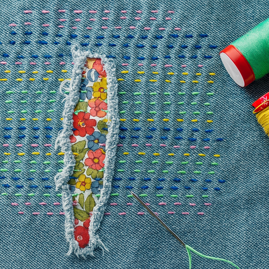 Visible Mending Jeans mit floralem Patch und bunten Sashiko-Stichen – kreative Reparatur mit Handarbeit.